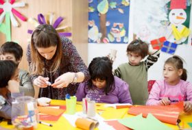 Female special education teacher working with a group of  special needs primary schoolchildren, she is showing them how to glue paper